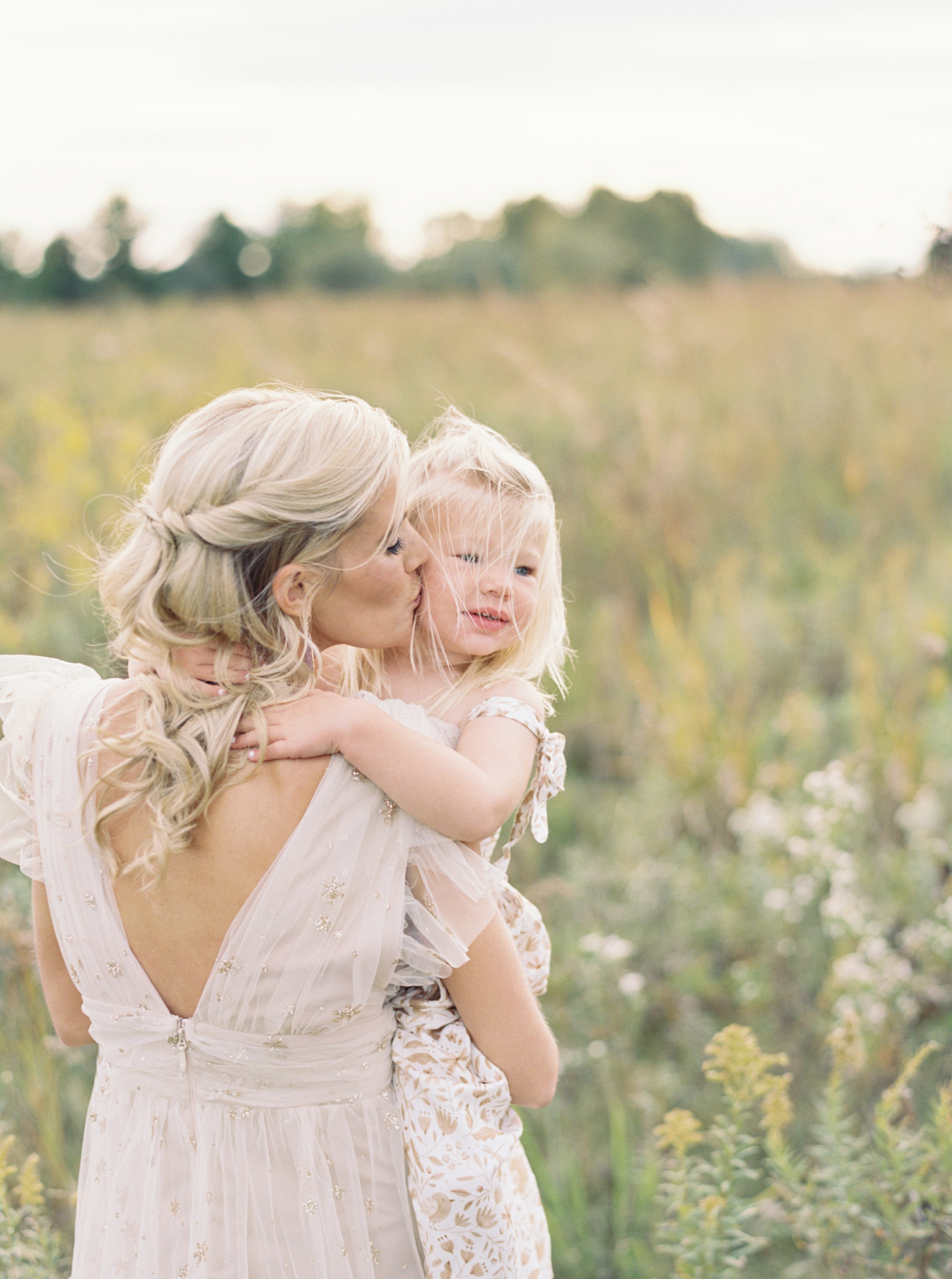 Mother and daughter cuddle and kiss in middleton grassy field