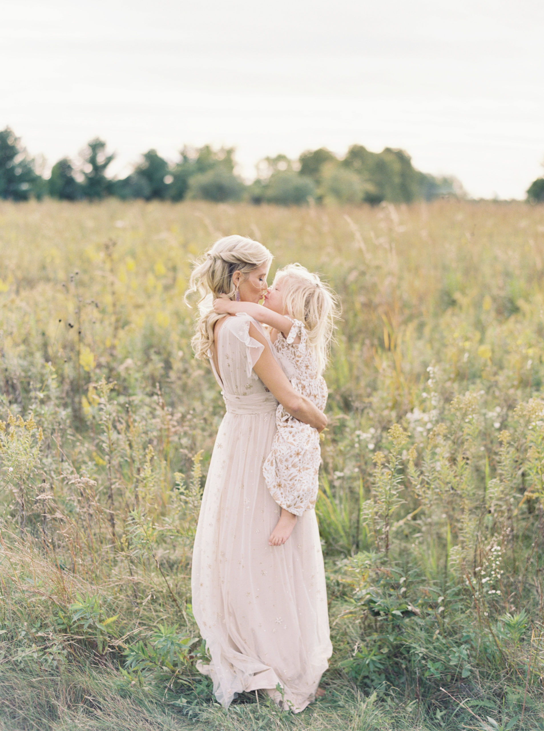 Mother and daughter cuddle and kiss in middleton grassy field