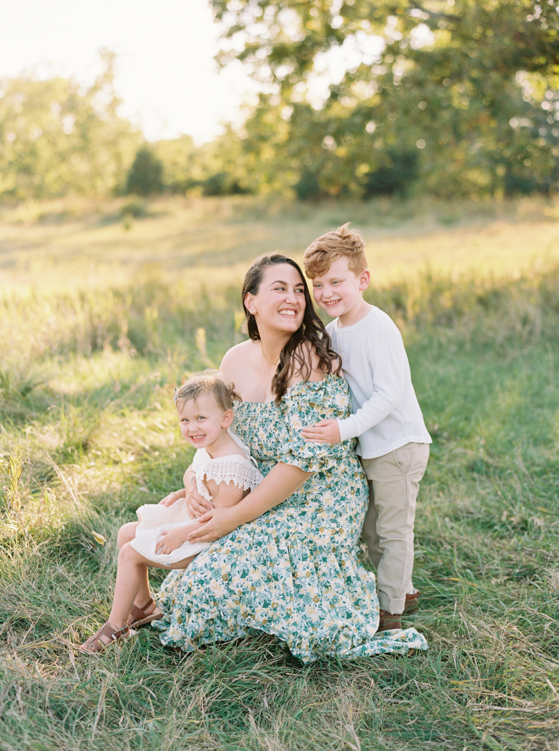 Mother, daughter, and son cuddling in a grassy green field setting in Shorewood in the summer