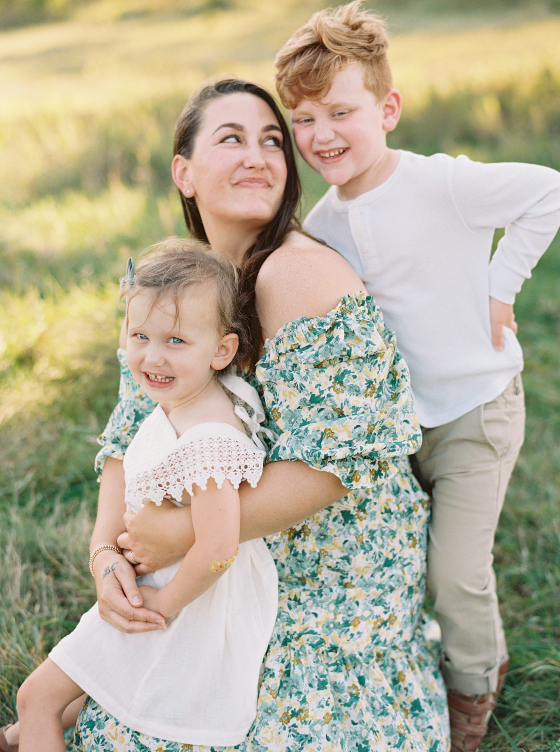 Mother, daughter, and son cuddling in a grassy green field setting in Shorewood in the summer