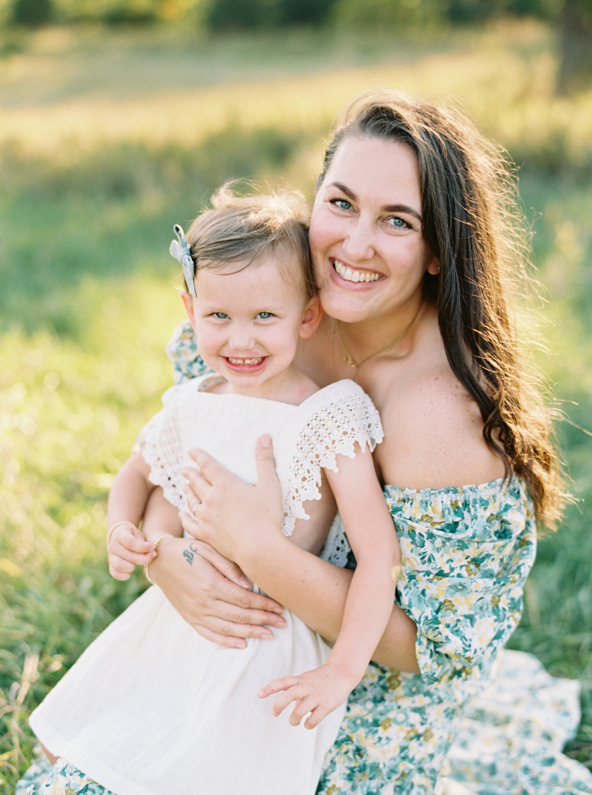 Mother and daughter cuddle in a grassy green field setting in Shorewood in the summer