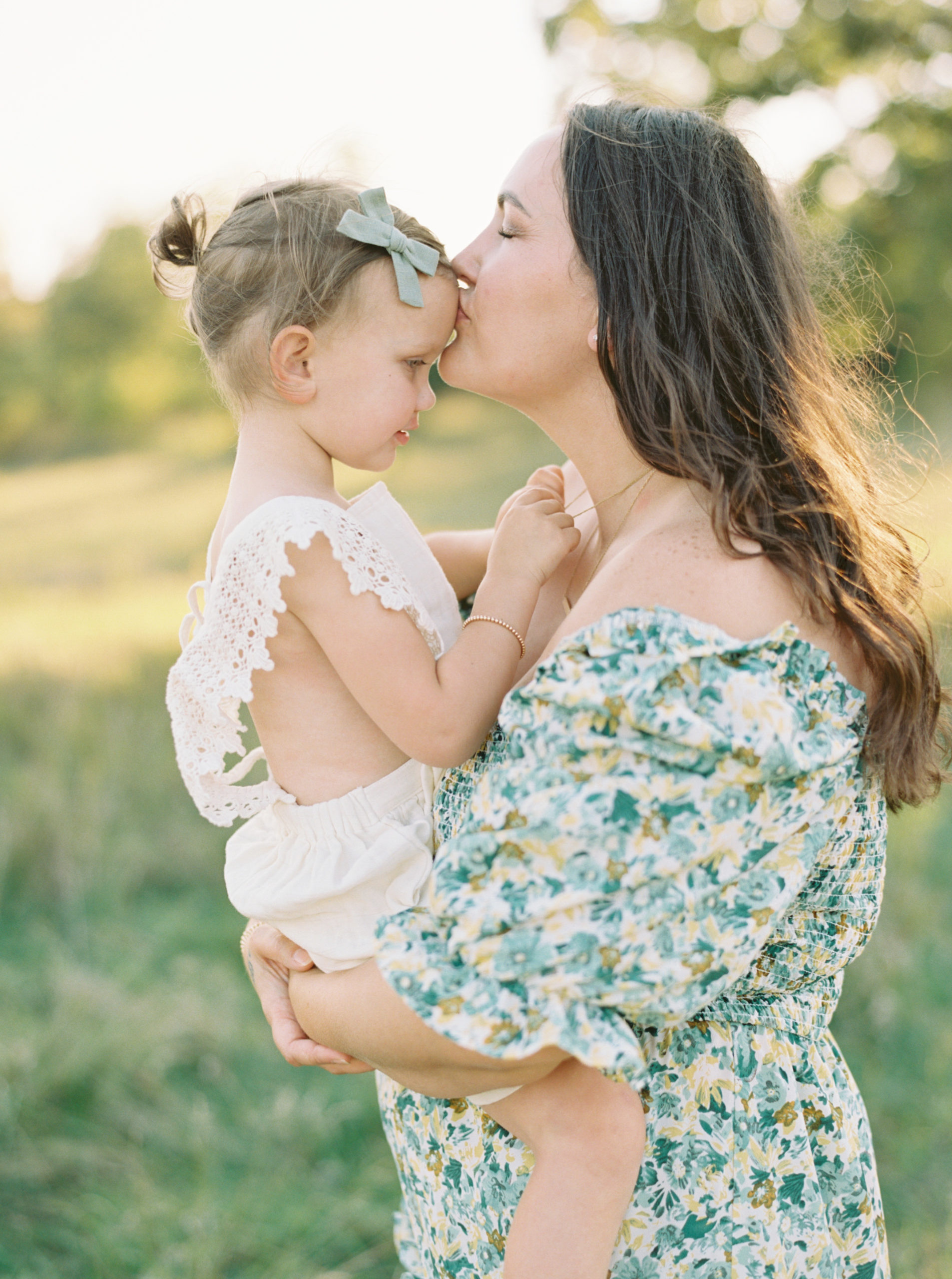 Mother and daughter cuddle in a grassy green field setting in Shorewood in the summer
