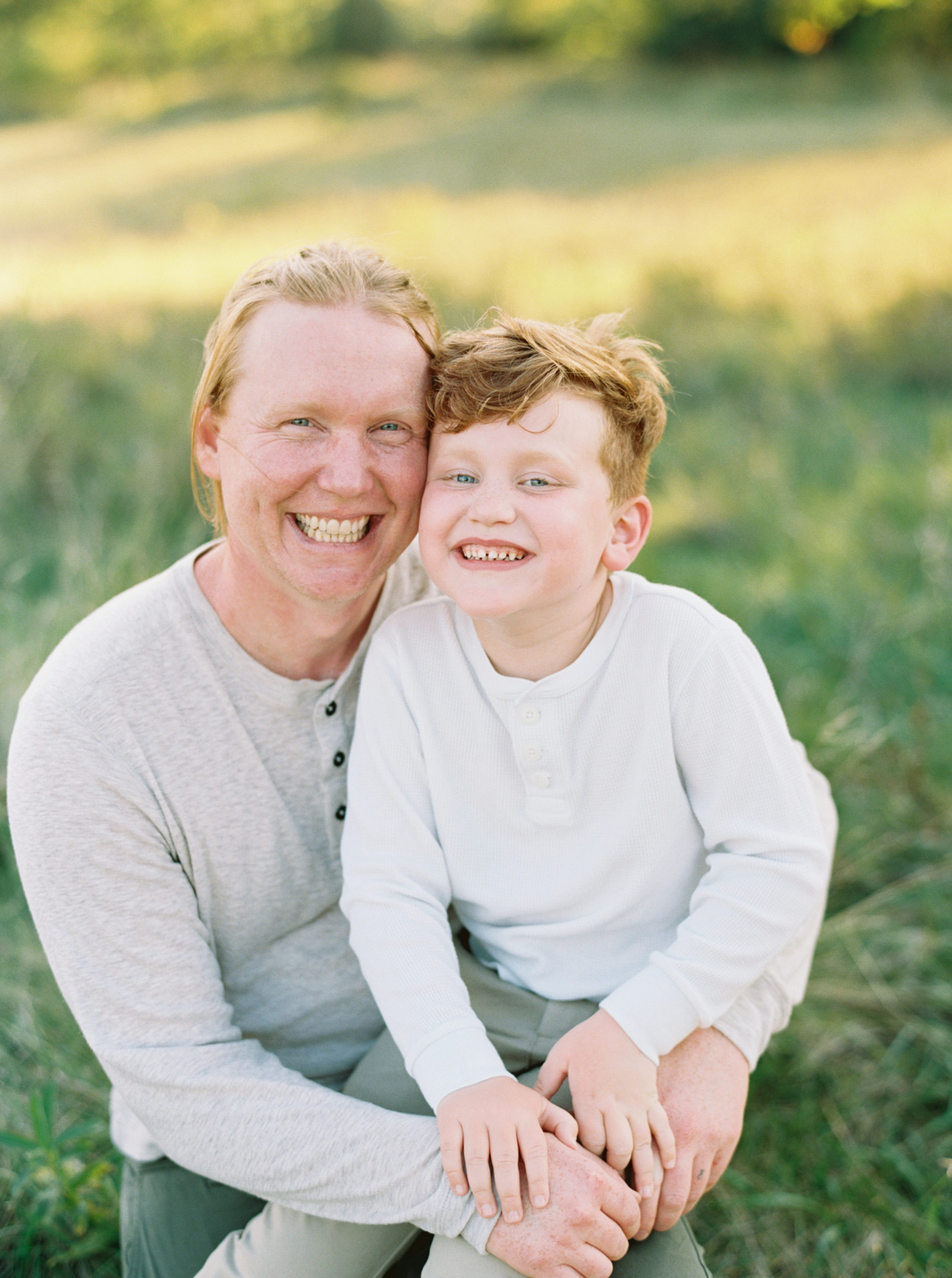 Father and Son cuddling in a grassy green field setting in Shorewood in the summer