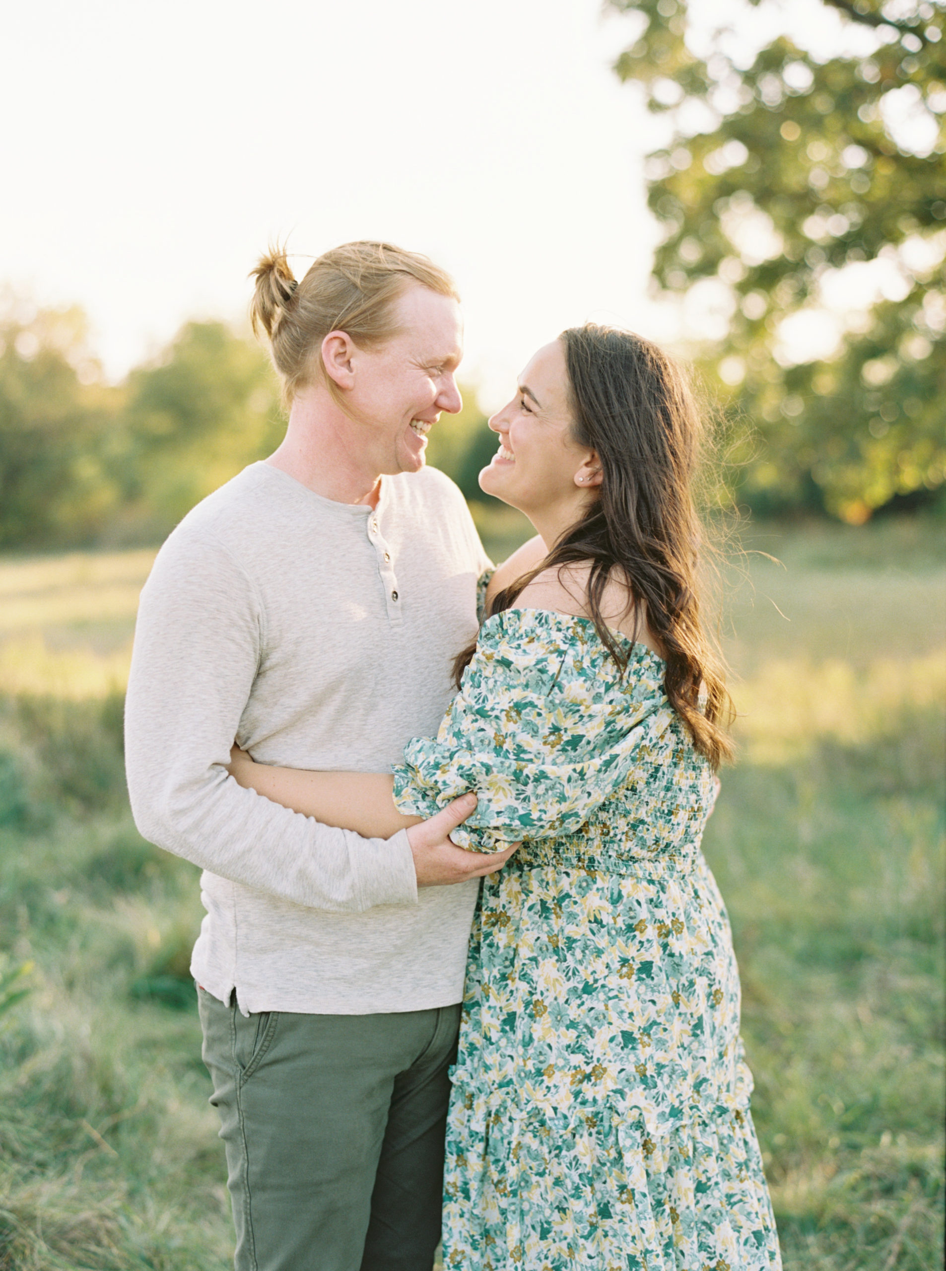 Husband and Wife cuddle in a grassy green field setting in Shorewood in the summer