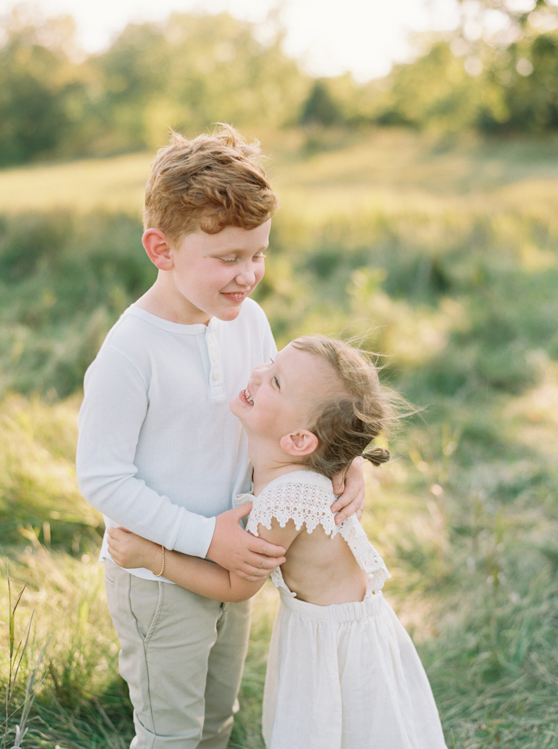 Brother and Sister cuddling in a grassy green field setting in Shorewood in the summer
