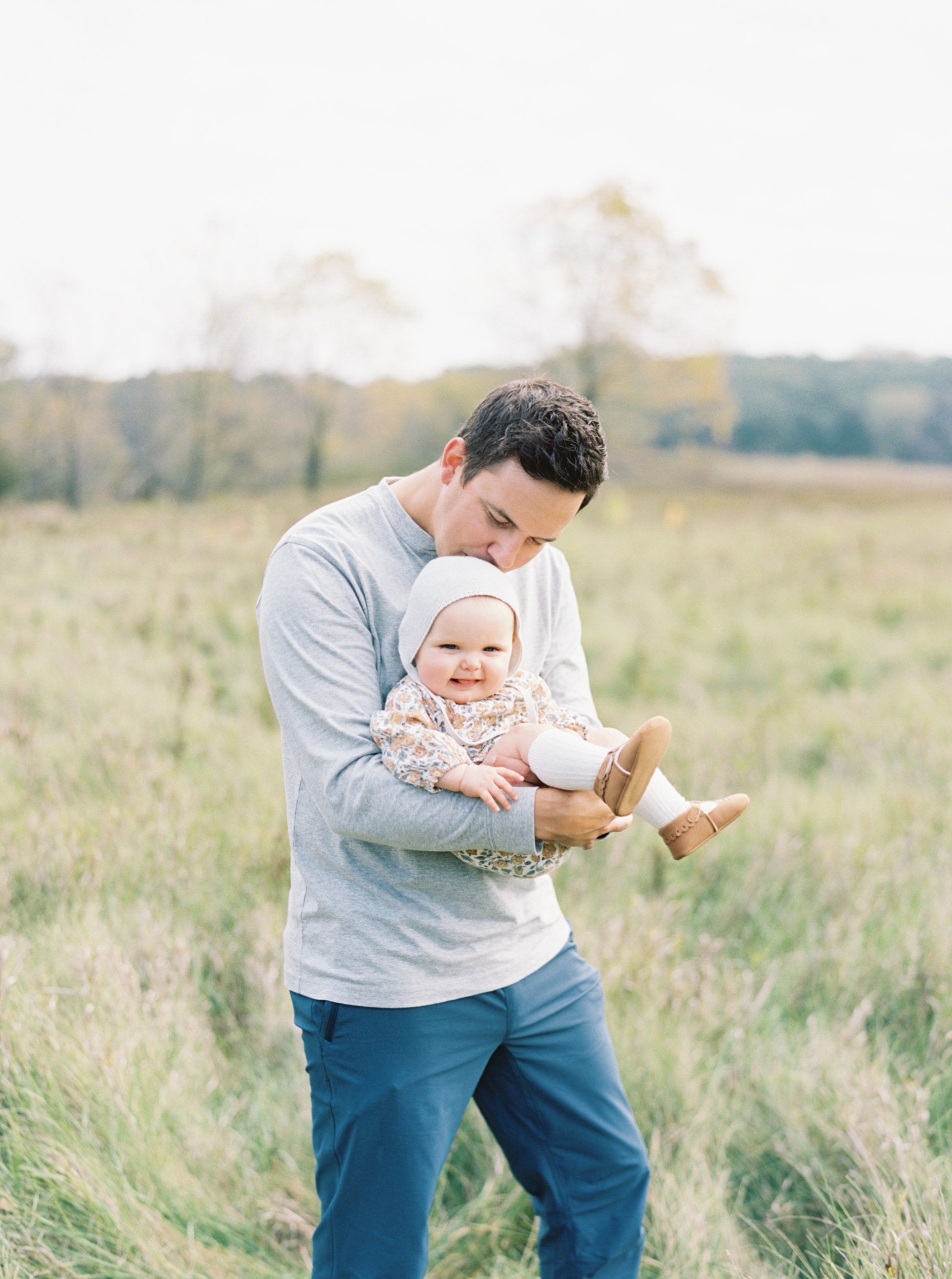 A father cuddles his baby in a grassy Hartland field on a beautiful Fall afternoon