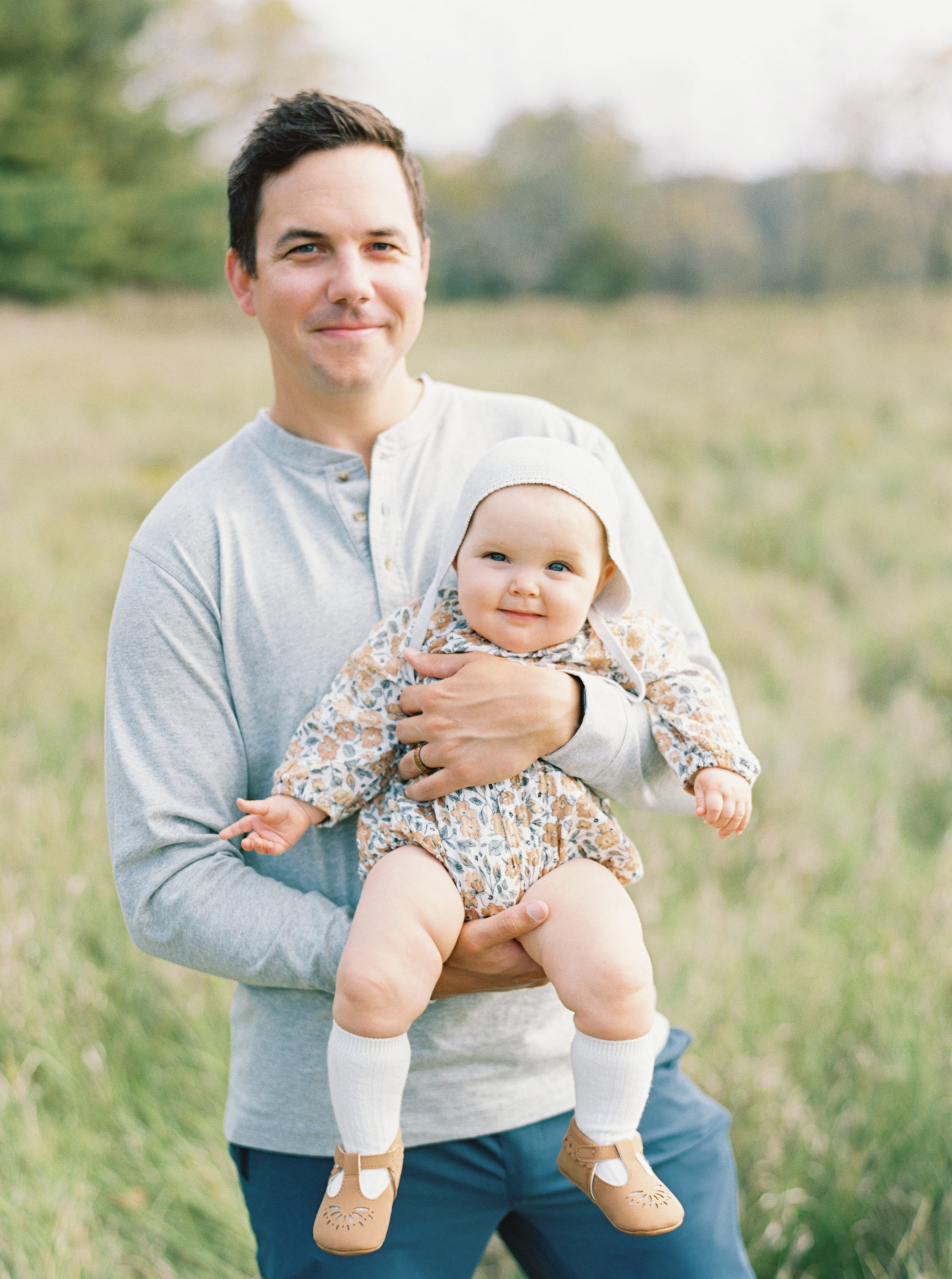 A father cuddles his baby in a grassy Hartland field on a beautiful Fall afternoon