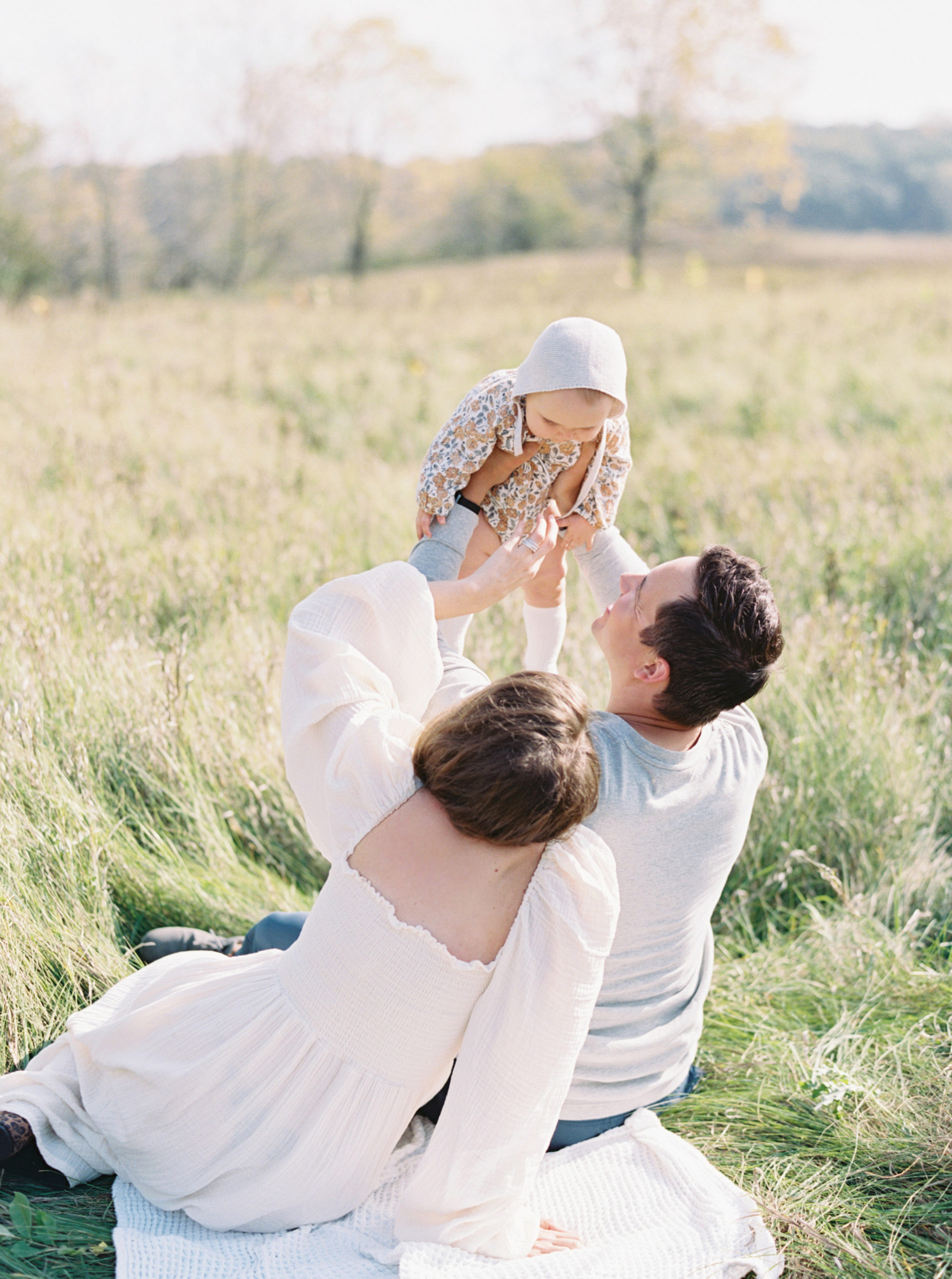A mother and father cuddle their baby in a grassy Hartland field on a beautiful Fall afternoon