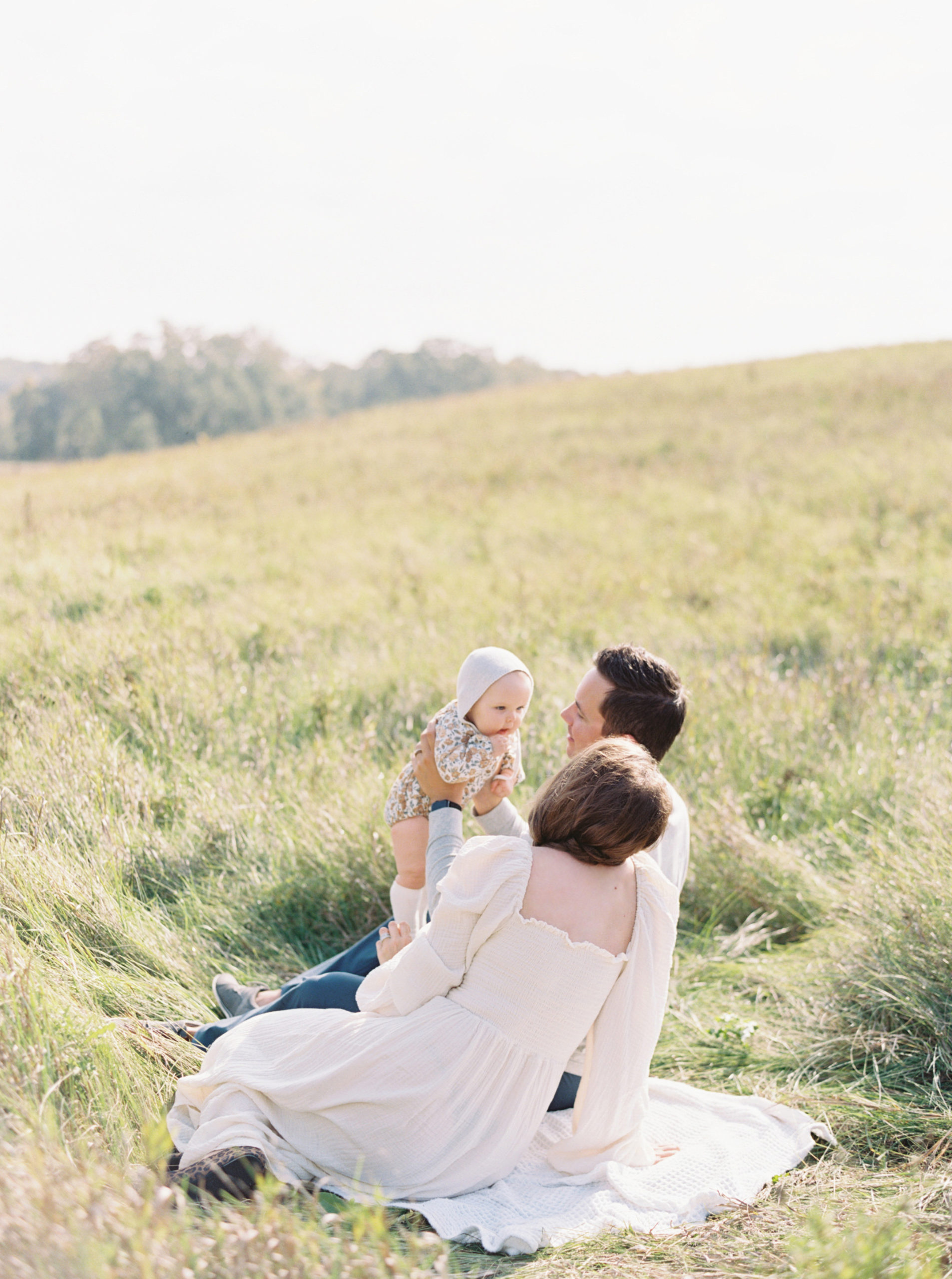 A mother and father cuddle their baby in a grassy Hartland field on a beautiful Fall afternoon