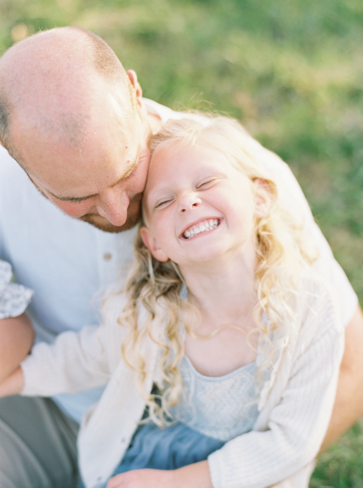 Father cuddles daughter in beautiful, green, grassy Milwaukee field