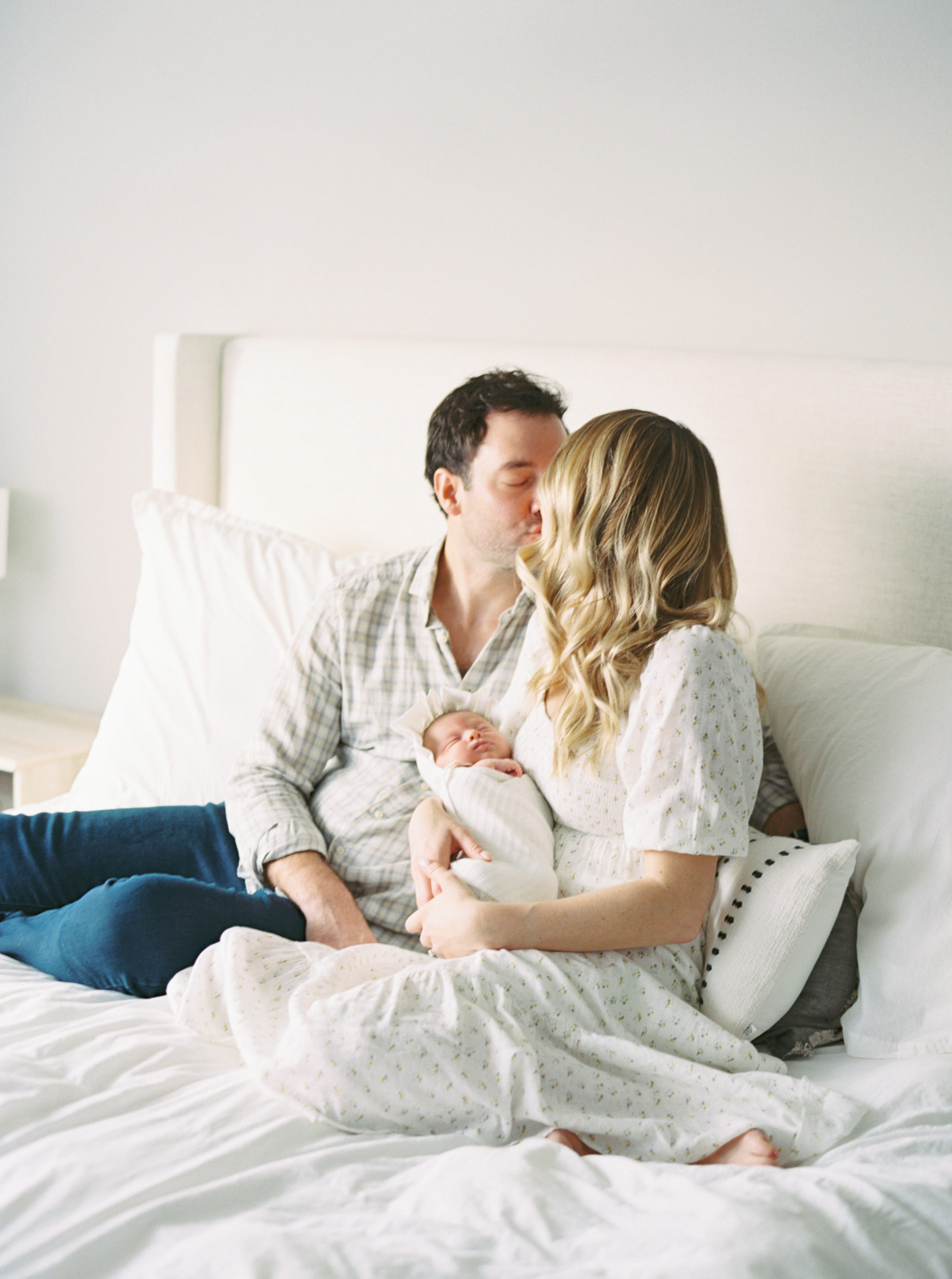 Mother and Father cuddling baby in a beautiful, bright, Milwaukee bedroom