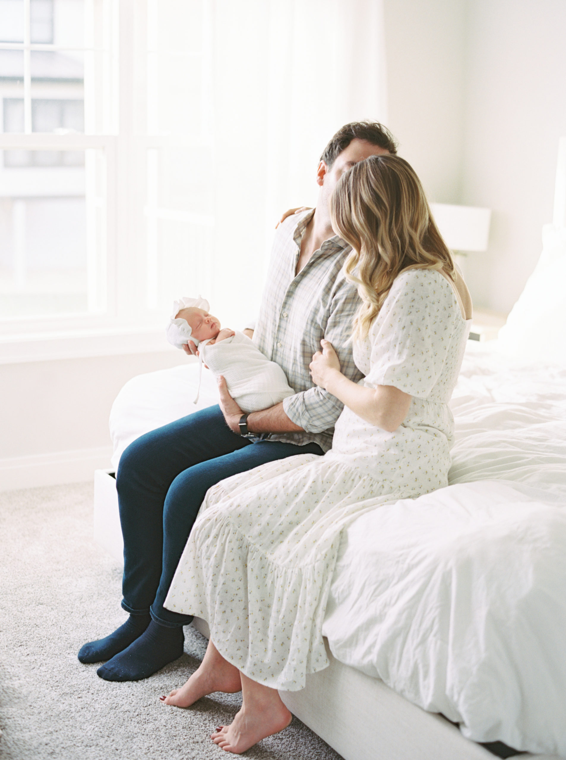 Mother and Father cuddling baby in a beautiful, bright bedroom