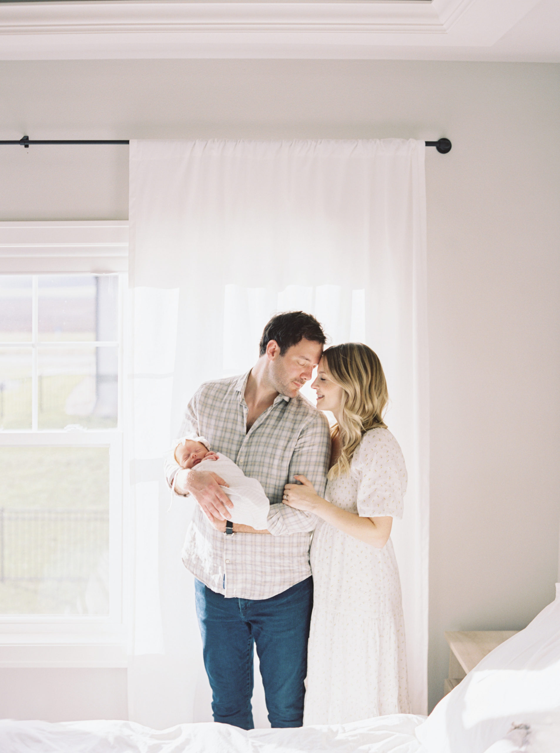 Mother and Father cuddling baby in a beautiful, bright bedroom