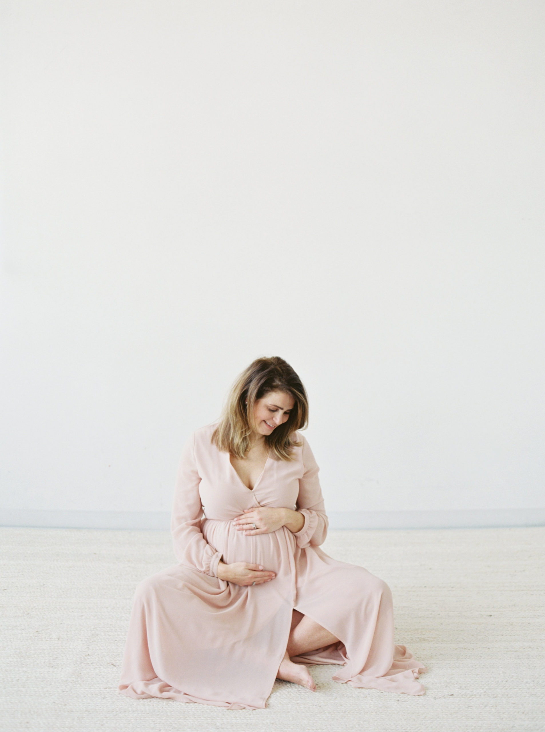 expecting mother in soft pink dress in white studio taken by Milwaukee maternity photographer talia laird photography