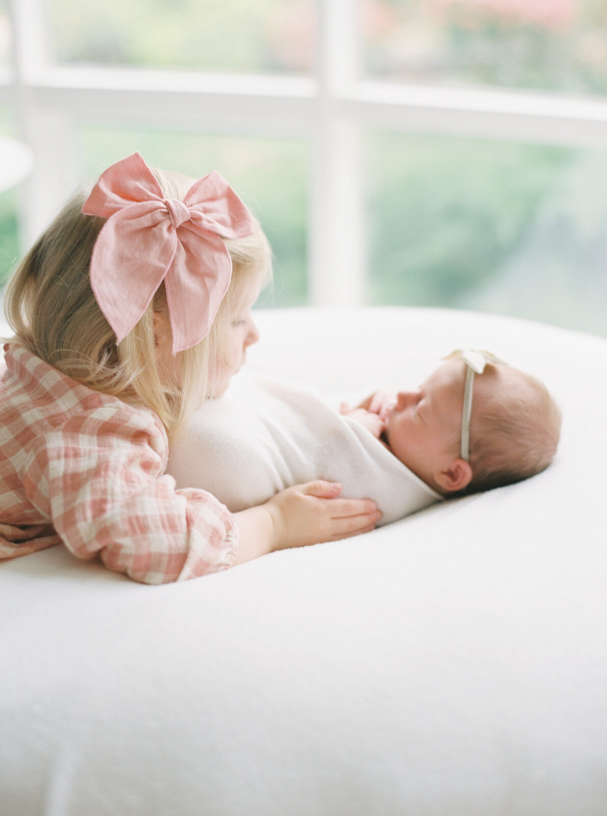 sister in a pink dress looking at a newborn baby girl during an in home newborn session with Talia Laird Photography