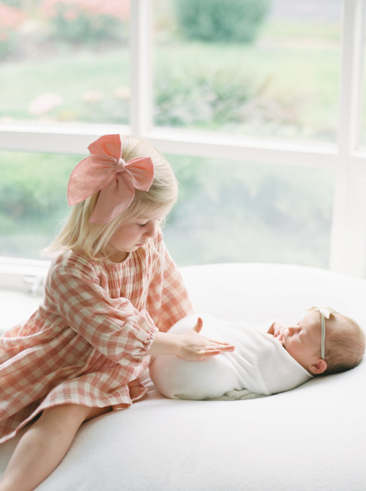 sister in a pink dress looking at a newborn baby girl during an in home newborn session with Talia Laird Photography